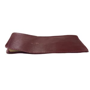 May include: A burgundy leather card holder. The holder is closed and lying on a white surface. The leather is smooth and appears to be high quality. The card holder is rectangular with slightly rounded corners. It is a simple design with no visible embellishments or branding.  The color is a deep, rich burgundy. The stitching is neat and even. The leather is supple and shows slight folds where it is bent. The card holder is compact and appears to be well-made. It would be suitable for carrying credit cards, business cards, or other small items.