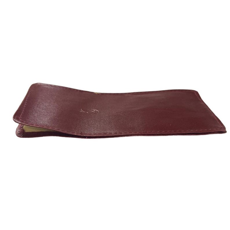 May include: A burgundy leather card holder. The holder is closed and lying on a white surface. The leather is smooth and appears to be high quality. The card holder is rectangular with slightly rounded corners. It is a simple design with no visible embellishments or branding.  The color is a deep, rich burgundy. The stitching is neat and even. The leather is supple and shows slight folds where it is bent. The card holder is compact and appears to be well-made. It would be suitable for carrying credit cards, business cards, or other small items.