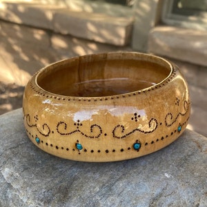 May include: A wooden bowl with a decorative design of brown dots and swirls. The bowl is decorated with turquoise blue stones.
