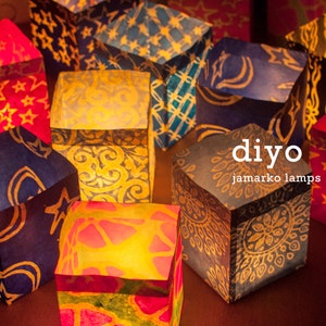 May include: A collection of colorful, illuminated paper lanterns. The lanterns are cube-shaped and decorated with various patterns, including stars and floral designs. The text "diyo jamarko lamps" is visible on the front of the lanterns.