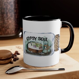 Op de afbeelding: Witte keramische mok met een zwarte rand en handvat. De mok heeft een aquarel-illustratie van een camper in een glazen pot met de tekst "GYPSY SOUL" erboven.