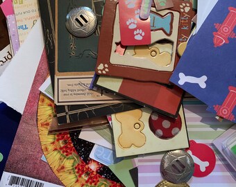 May include: A collection of colorful paper scraps, stickers, and embellishments for scrapbooking and crafting. The scraps feature various designs, including paw prints, bones, and a fire hydrant. There are also several metal buttons with a decorative design.