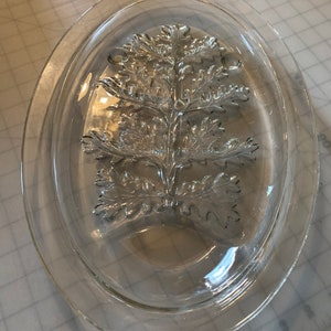 May include: A clear glass oval dish with a raised design of a leafy branch in the center.