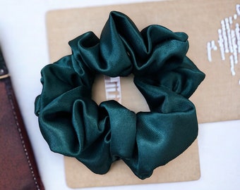 May include: A dark green satin scrunchie hair tie. The scrunchie is made of soft, silky fabric and is perfect for adding a touch of elegance to any hairstyle.