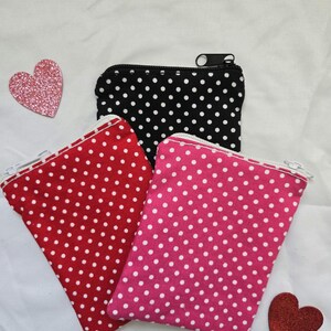May include: Three small zippered pouches in red, black, and pink, each with a white polka dot pattern. The pouches have white zippers and are arranged on a white surface. Two glittery heart-shaped decorations are also present.