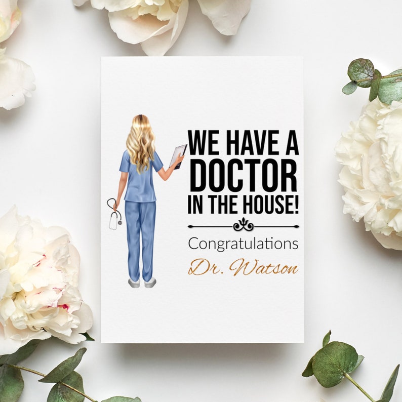 May include: A white card with a black and white illustration of a woman in a blue medical uniform holding a stethoscope and a tablet. The text on the card reads "We have a doctor in the house! Congratulations Dr. Watson".