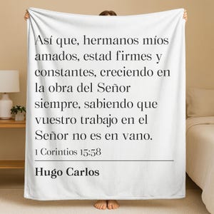 May include: A white fleece blanket featuring black printed text in Spanish that reads: Así que, hermanos míos amados, estad firmes y constantes, creciendo en la obra del Señor siempre, sabiendo que vuestro trabajo en el Señor no es en vano. 1 Corintios 15:58 Hugo Carlos.