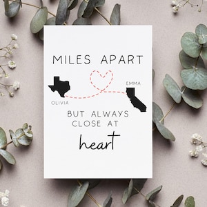 May include: A white card with the text "MILES APART BUT ALWAYS CLOSE AT heart." The card features black silhouettes of Texas and California, connected by a red heart-shaped line. Names "Olivia" and "Emma" are placed near the states.