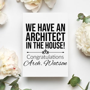 May include: A white card with black text that reads "We have an architect in the house!" with a decorative flourish and the text "Congratulations Arch. Watson". The card is surrounded by white flowers and green leaves.