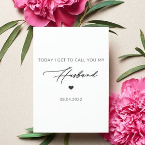 May include: White card with the text "TODAY I GET TO CALL YOU MY HUSBAND" in black script font with a small black heart below the text. The date "08.04.2022" is printed below the heart. The card is surrounded by pink flowers and green leaves.
