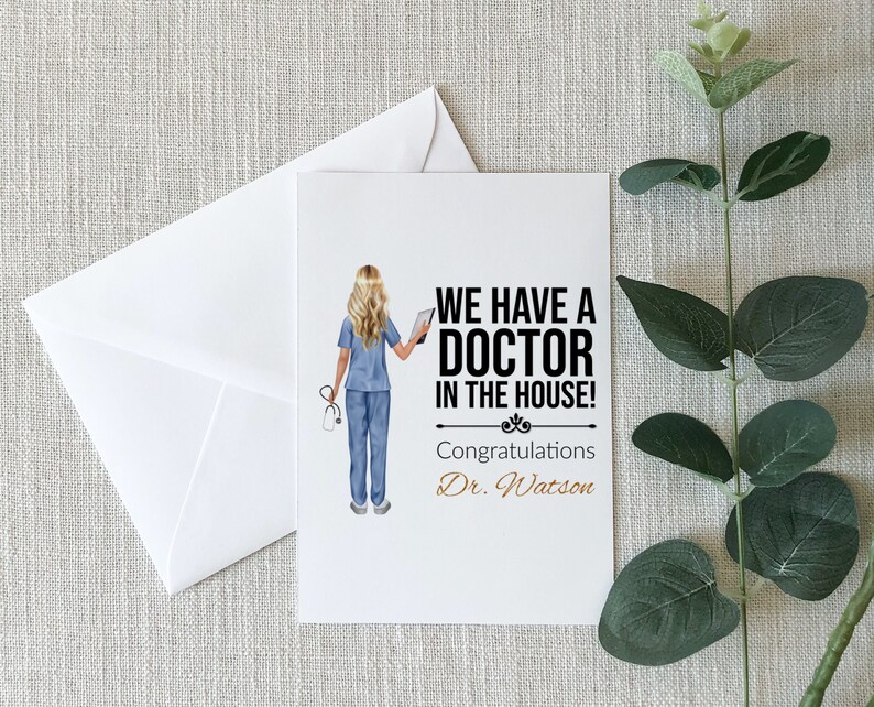 May include: A white card with a black and white illustration of a woman in a blue medical uniform holding a tablet. The text on the card reads "We have a Doctor in the house! Congratulations Dr. Watson."