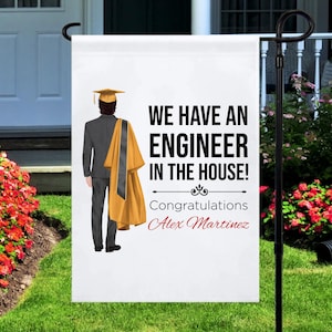 May include: A white graduation yard sign with a black silhouette of a person wearing a graduation cap and gown. The sign reads "We have an engineer in the house! Congratulations Alex Martinez."