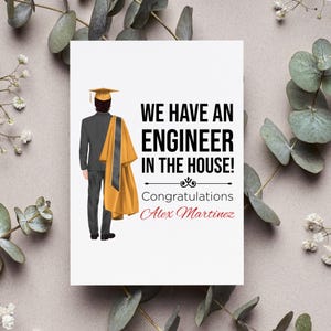 May include: A white graduation card with the text "WE HAVE AN ENGINEER IN THE HOUSE!" and "Congratulations Alex Martinez" in red script. An illustration of a graduate in a cap and gown is on the left.