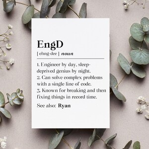 May include: A white card with the definition of "EngD" printed in black. The definition includes the pronunciation, a description of an engineer, and the name "Ryan". The card is surrounded by eucalyptus leaves and small white flowers.
