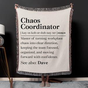 May include: A woven throw blanket with fringed edges featuring the black text Chaos Coordinator, a phonetic pronunciation, the noun classification, and a definition describing a master of turning workplace chaos into clear direction. See also: Dave.