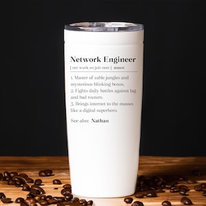May include: A white travel mug with a black lid, featuring the definition of "Network Engineer." The text includes the phonetic pronunciation, a list of job duties, and the name "Nathan." The mug is on a wooden surface with scattered coffee beans.