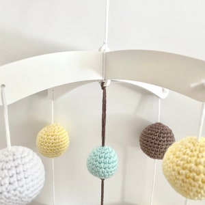 May include: A white wooden mobile arm with five crocheted balls hanging from it. The balls are yellow, white, brown, and light blue.