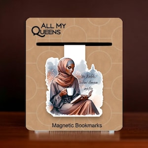 May include: A magnetic bookmark featuring a woman wearing a hijab and holding a book and a cup. The background is a watercolor-style painting with a quote in Arabic script that reads "Ya Rabbi, zidni ilman nafia". The bookmark is labeled "Magnetic Bookmarks" and "All My Queens".