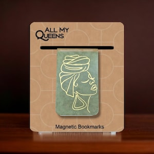 May include: A gold magnetic bookmark with a green background featuring a line drawing of a woman with a headscarf. The bookmark has the text "All My Queens" at the top and "Magnetic Bookmarks" at the bottom.