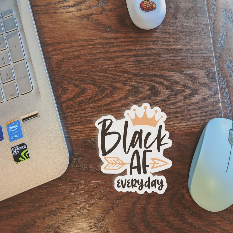 May include: A white sticker with a black and orange design. The sticker says "Black AF Everyday" with a crown above the word "Black" and an arrow pointing to the right of the word "AF".