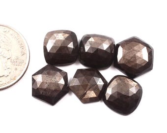 Pode incluir: Seis pedras preciosas castanho-escuras facetadas com formato quadrado ou hexagonal são exibidas em um fundo branco. As pedras preciosas têm uma superfície polida e reflexiva. Uma moeda de um quarto de dólar dos EUA é visível para comparação.