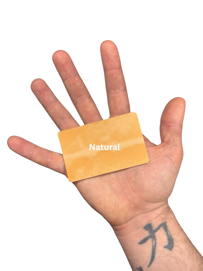 Puede incluir: Una tarjeta rectangular con una superficie texturizada de color naranja claro que presenta la palabra Natural impresa en blanco en el centro. La tarjeta tiene esquinas redondeadas y un acabado mate, con un tono uniforme en toda su superficie.
