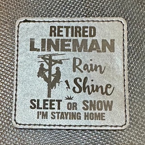 May include: A black leather patch with white stitching and the text "Retired Lineman Rain or Shine Sleet or Snow I'm Staying Home". The patch features a silhouette of two linemen working on a power line.