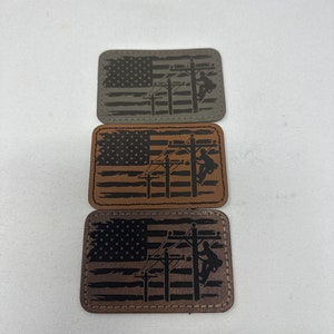 May include: Three leather patches with an American flag design and a silhouette of a person working on a power line. The patches are in different shades of brown, gray, and tan.