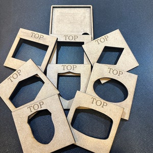 Op de afbeelding: Zeven houten vierkanten met uitgesneden vormen en het woord "TOP" erop gedrukt. De vierkanten zijn op elkaar gestapeld.