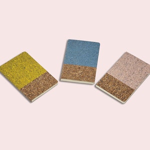 May include: Three small notebooks with cork covers. The notebooks are yellow, blue, and pink.
