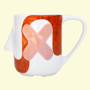 May include: White ceramic mug with a brown woodgrain design and a large pink bandage on the front.