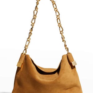 Może przedstawiać: Brązowa zamszowa torba na ramię ze złotym łańcuszkiem. Torba ma luźny design i złote akcenty w miejscu mocowania paska. Łańcuch składa się z dużych, zazębiających się ogniw.