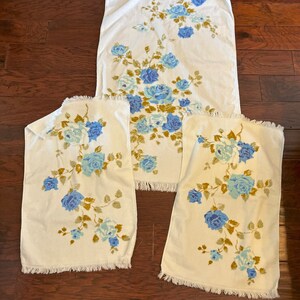 May include: Set of three white towels with blue and green floral pattern. The towels have a fringed edge.