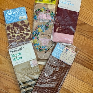 May include: An assortment of vintage knee-high socks in their original packaging. Styles include leopard print, floral, striped, and patterned designs. The packaging includes text such as "Fun Knee Hi's" and "Fits Sizes 9-11".