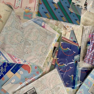 Peut inclure: Un assortiment de papiers d'emballage aux motifs color&eacute;s, dont un motif bleu et vert avec des canards, un motif bleu et blanc avec des arcs-en-ciel et un motif bleu clair avec des past&egrave;ques. Le papier d'emballage est emball&eacute; dans des sacs en plastique transparents et &eacute;tiquet&eacute; avec des prix.