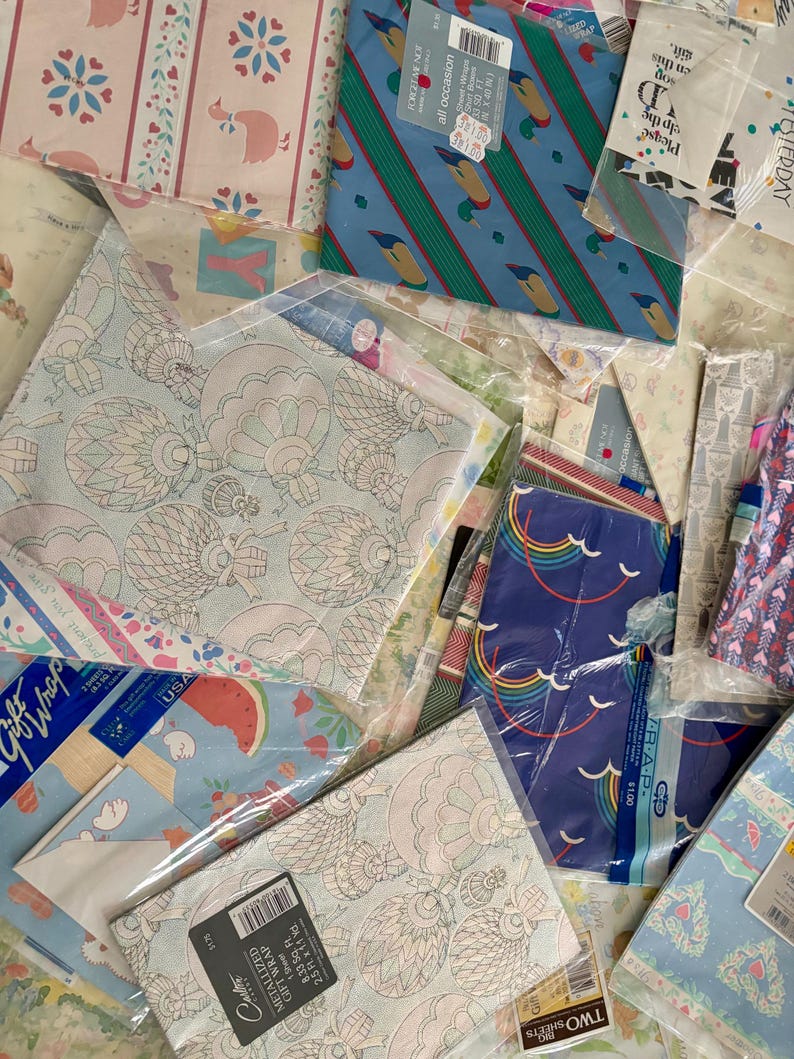 Peut inclure: Un assortiment de papiers d'emballage aux motifs color&eacute;s, dont un motif bleu et vert avec des canards, un motif bleu et blanc avec des arcs-en-ciel et un motif bleu clair avec des past&egrave;ques. Le papier d'emballage est emball&eacute; dans des sacs en plastique transparents et &eacute;tiquet&eacute; avec des prix.