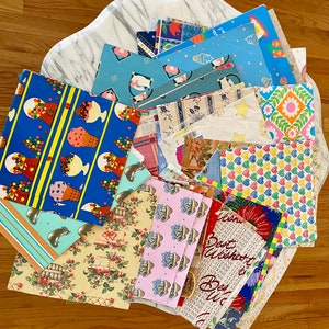 Peut inclure: Un assortiment de papiers d'emballage color&eacute;s avec diff&eacute;rents motifs, notamment des cornets de glace, des c&oelig;urs, des fleurs et des &eacute;toiles. Le papier est dispos&eacute; en pile sur une surface en marbre blanc.