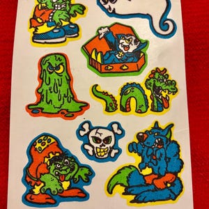 May include: A sheet of vintage Halloween stickers featuring a variety of spooky characters, including a ghost, a vampire, a monster, a dragon, a skull, and a werewolf. The stickers are printed on white paper with a bright, colorful design.