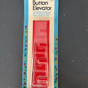 May include: A red Button Elevator tool for sewing, packaged in a blue and white card with floral accents. The card reads "Button Elevator" and "4 Standard Elevations for Effortless Sewing From Sheers to Furs."