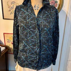 May include: A long-sleeved button-down shirt with a black background and a colorful, intricate pattern. The pattern includes teal, purple, and orange accents. The shirt has a black collar and is displayed on a vintage dress form.
