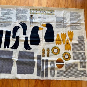 May include: A white fabric panel featuring printed sewing patterns for a crow doll titled AS THE CROW FLIES and MR. CROW. The sheet includes black crow body parts, yellow feet, sunflower motifs, and gray patterned fabric sections for clothing.