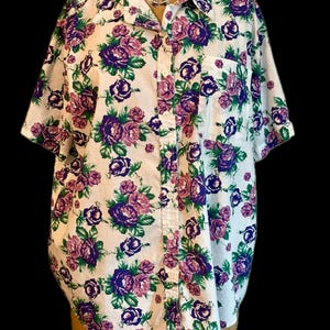 May include: A white button-down shirt with a short sleeve and a floral pattern of purple and green roses.