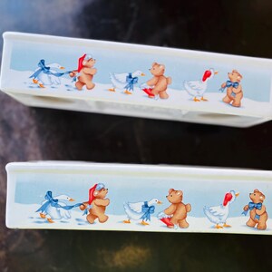 May include: Two rectangular ceramic dishes with a winter scene. The design features brown teddy bears in Santa hats and geese with blue bows. The background is a light blue with white snow.