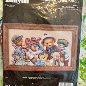 May include: A Janlynn Counted Cross Stitch kit featuring a framed image of a group of teddy bears wearing hats and outfits. The finished size is 14" x 8" (35.6 x 20.3 cm). The kit includes cotton Aida fabric, floss, beads, needles, and instructions.