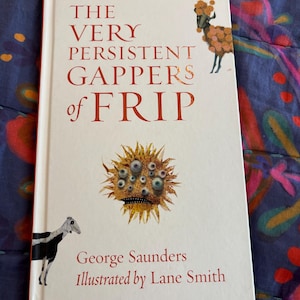 May include: A hardcover book titled "The Very Persistent Gappers of Frip" by George Saunders, illustrated by Lane Smith. The cover is white with red text and illustrations of a sheep and a spiky, eye-covered creature.