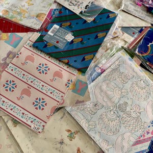 Peut inclure: Un assortiment de papiers d'emballage aux motifs color&eacute;s, dont un motif bleu et vert avec des canards, un motif rose et blanc avec des c&oelig;urs et des &eacute;toiles, et un motif bleu clair avec un motif floral. Le papier d'emballage est emball&eacute; dans des sacs en plastique transparents.