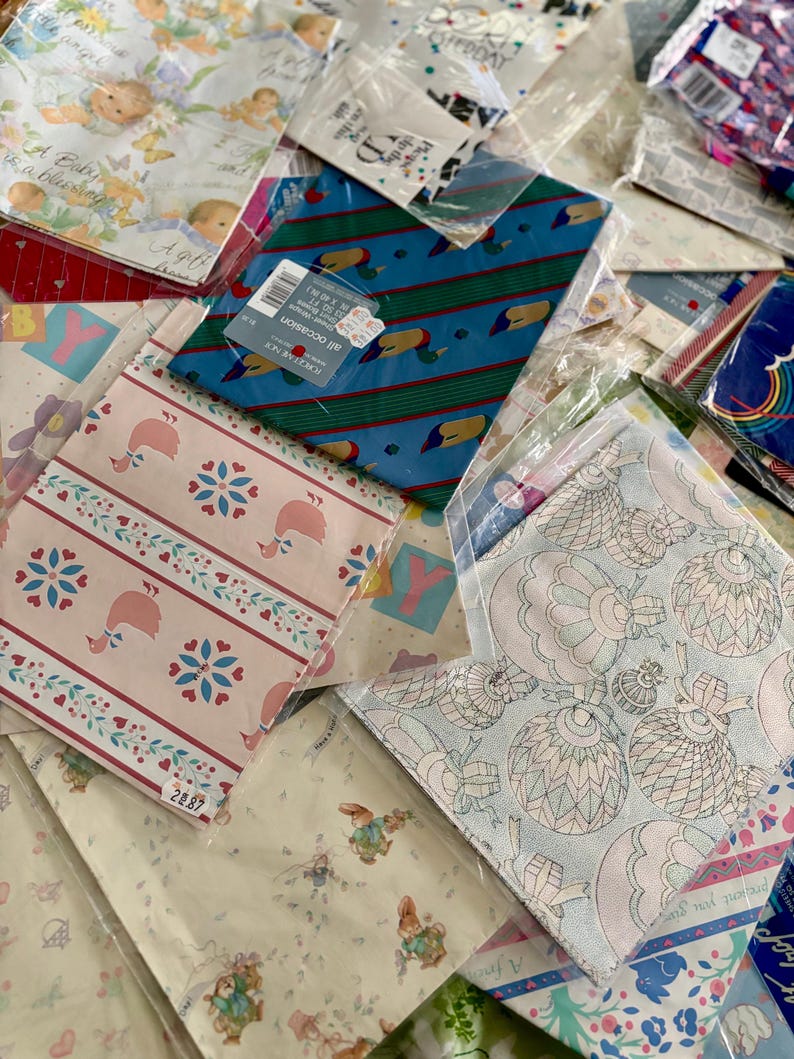 Peut inclure: Un assortiment de papiers d'emballage aux motifs color&eacute;s, dont un motif bleu et vert avec des canards, un motif rose et blanc avec des c&oelig;urs et des &eacute;toiles, et un motif bleu clair avec un motif floral. Le papier d'emballage est emball&eacute; dans des sacs en plastique transparents.