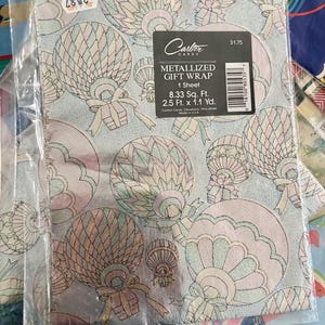 Peut inclure: Un rouleau de papier cadeau m&eacute;tallis&eacute; avec un fond bleu et un motif de montgolfi&egrave;res roses et vertes. Le papier cadeau mesure 8,33 pieds carr&eacute;s et 2,5 pieds sur 1,1 yard. Le texte "Carlton Cards" et "Metallized Gift Wrap" est imprim&eacute; sur le papier cadeau.
