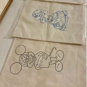 May include: Three white fabric panels with blue embroidery of cartoon characters. The top panel features a cartoon dwarf, the middle panel features Mickey Mouse, and the bottom panel features Mickey Mouse's head and body.
