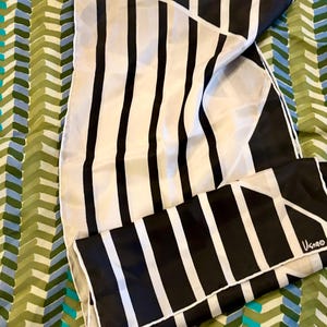 May include: A white and black striped silk scarf with a geometric design. The scarf is folded and has the word "Usagi" printed on the bottom right corner.
